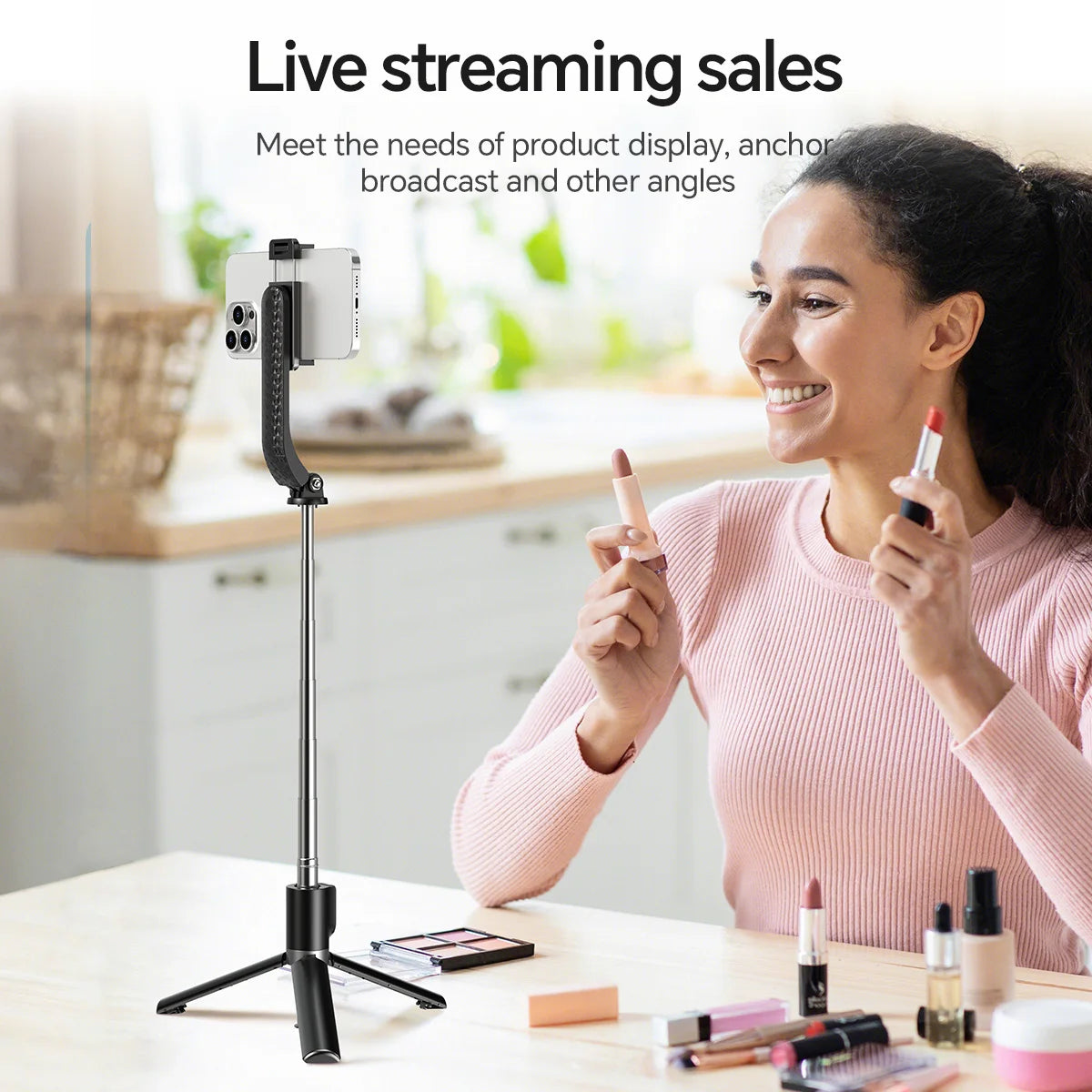 Woman using a smartphone on a selfie stick with makeup products on a table.
