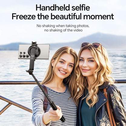Two women taking a selfie with a handheld selfie stick by a body of water.